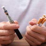 Man,Holding,Vape,And,Tobacco,Cigarette,Over,Desk